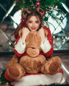 Young woman in Santa outfit hugging a teddy bear, exuding festive cheer.